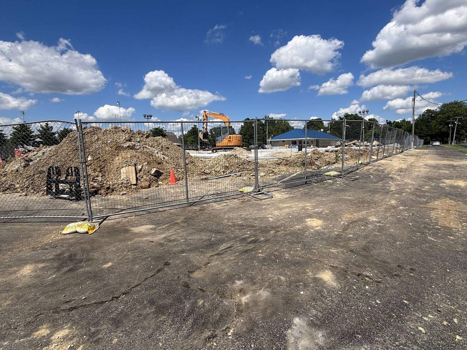 Temporary fence panels around a cleared dirt lot with an excavator working inside
