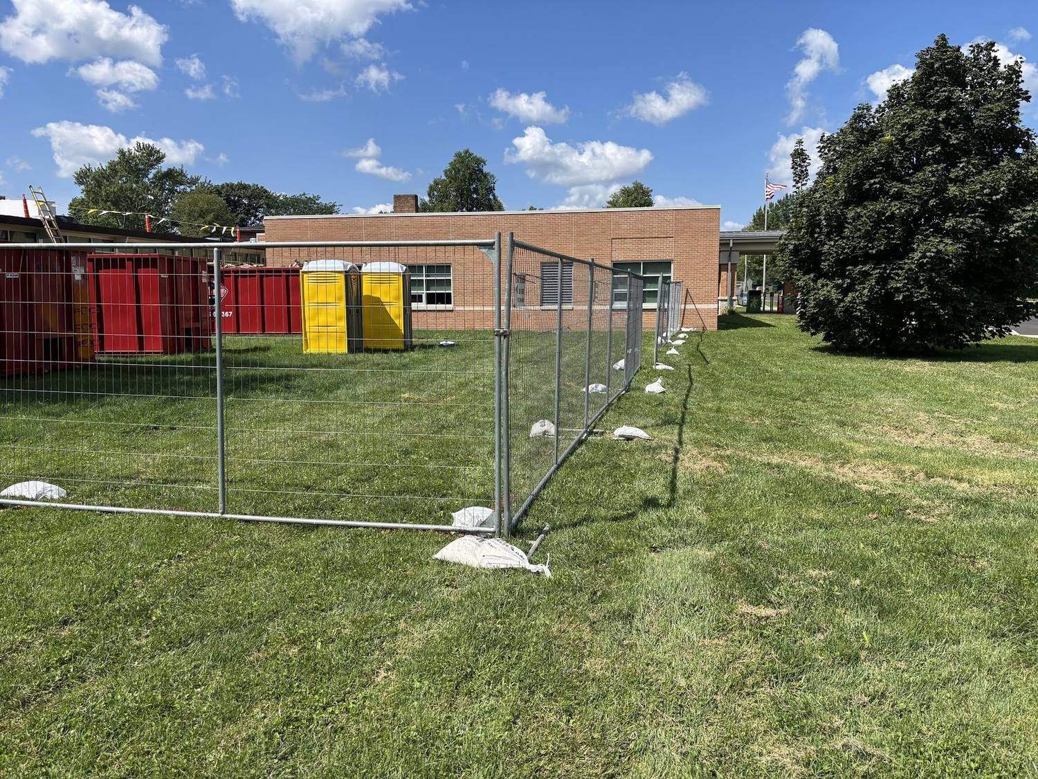 Temporary fence panels around a school building with dumpsters and site toilets inside the perimeter