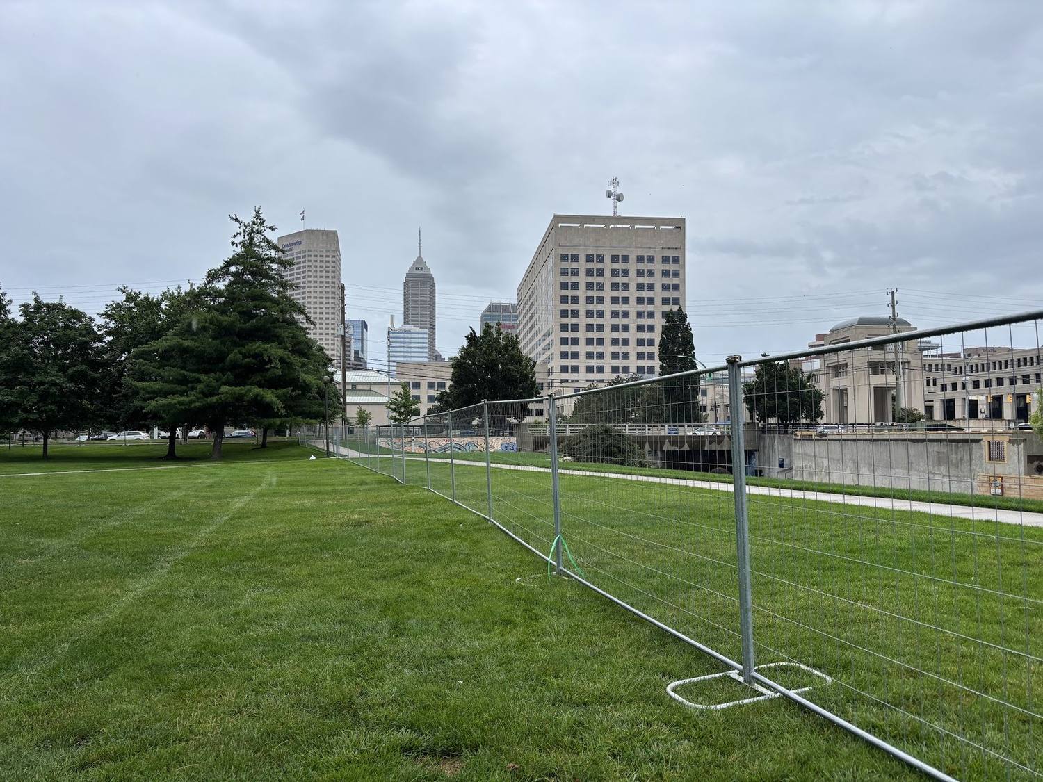 Temporary fence panels set on grass with the downtown Indianapolis skyline behind them