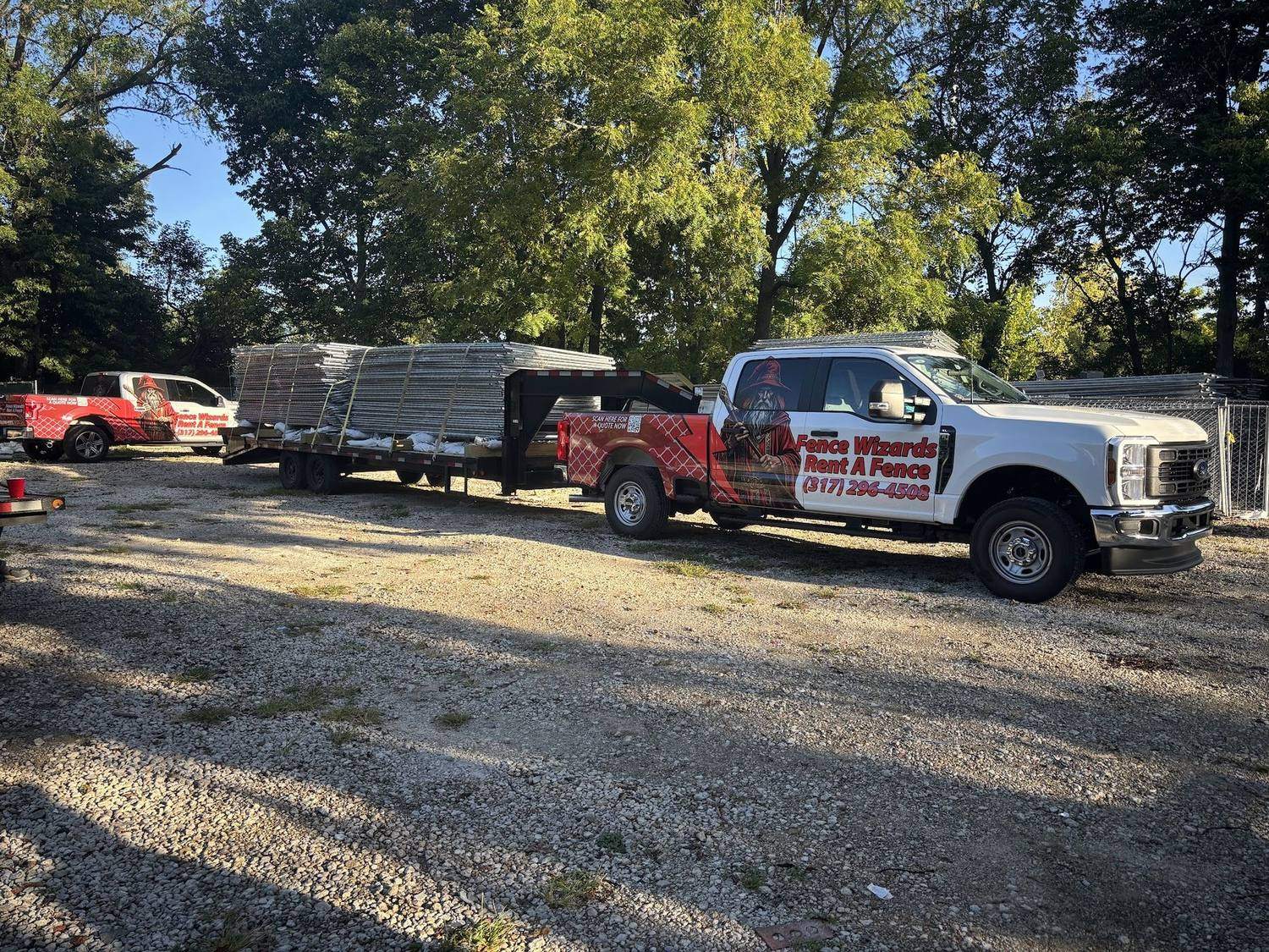 Two wrapped Fence Wizards trucks with loaded fence trailers on a gravel yard